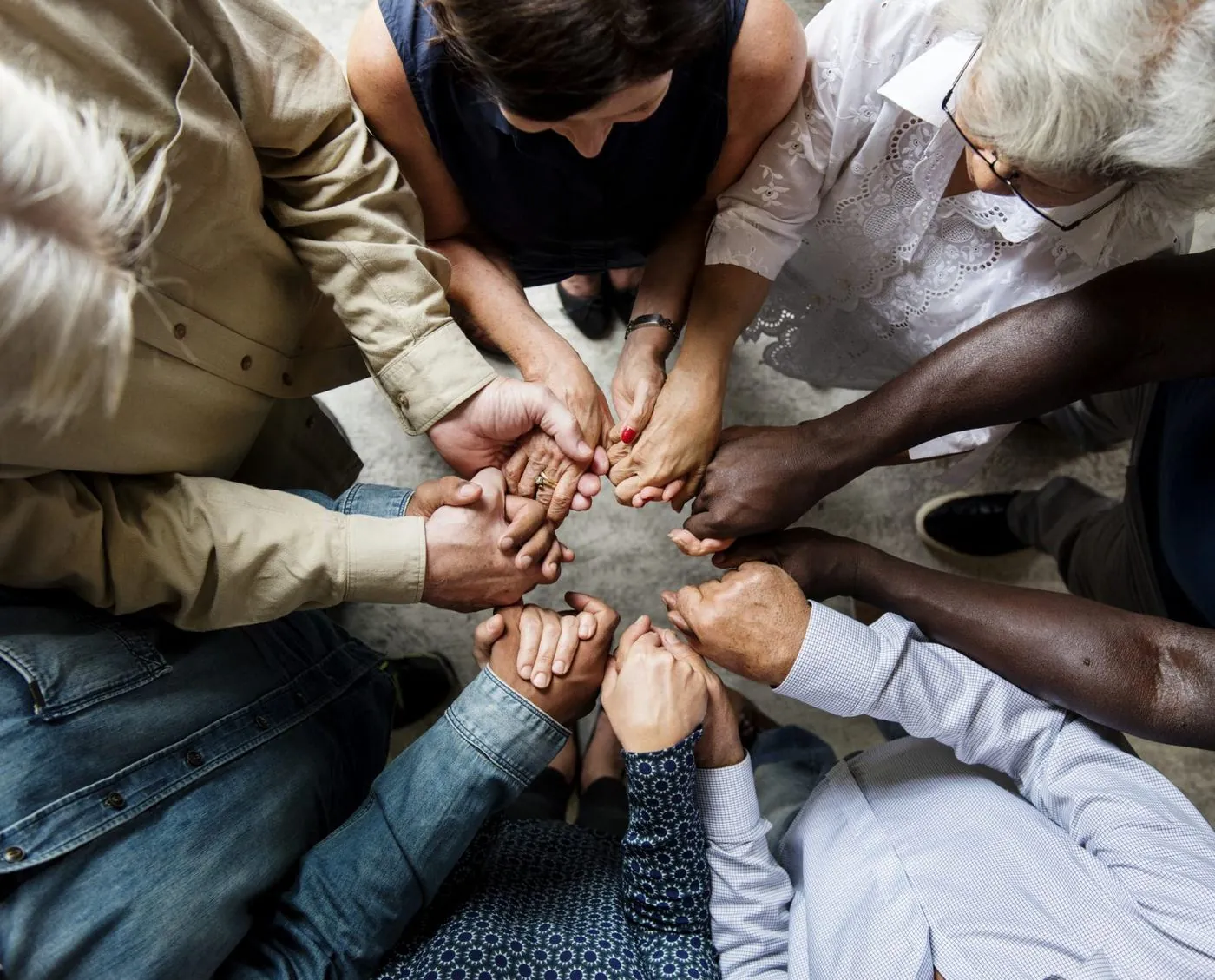 A circle of neighbors from different generations and backgrounds joining hands in prayer